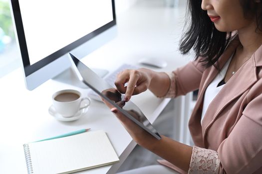 Asian businesswoman sitting in modern workplace and using digital tablet.