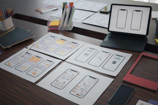 Digital tablet and wireframe sketches for mobile application on wooden table at creative office.