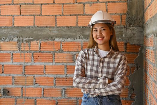 Confident architect woman in helmet standing with arm crossed at construction site. Industry, Engineer, construction concept.