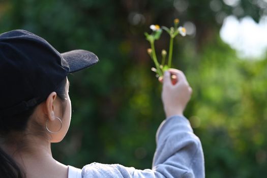 Rear view of young woman hand holding young plant on blur green nature background. Earth day concept.