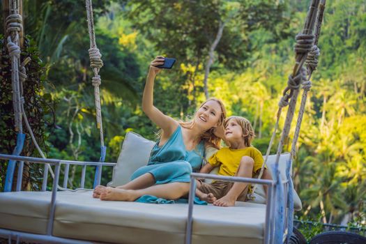 Mother and son swinging in the jungle rainforest of Bali island, Indonesia. Swing in the tropics. Swings - trend of Bali. Traveling with kids concept. What to do with children. Child friendly place.