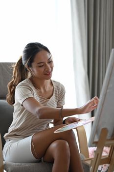 Attractive young woman spending leisure time at home and painting with watercolors.