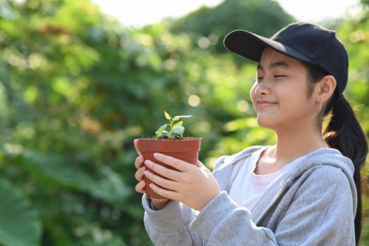Cute asian girl closed eyes while holding a plant in her hands. Saving the world, earth day concept.