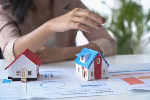 Small house model on white office desk and real estate agent sitting in background.