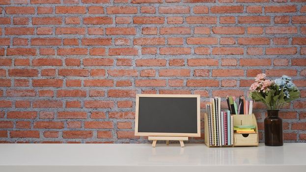Blank small blackboard and supplies on white table against brick wall with copy space for your text message or product isolated.