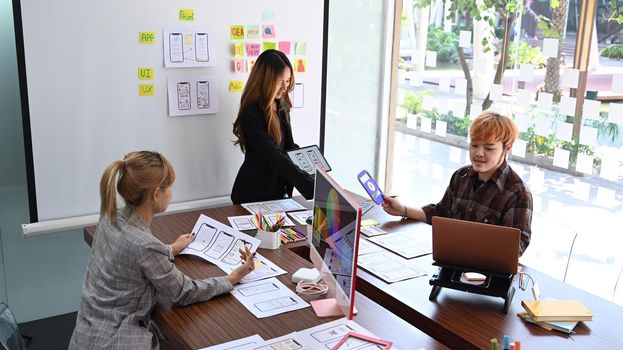 Creative people are brainstorming and planning about mobile app interface wireframe design together at office.