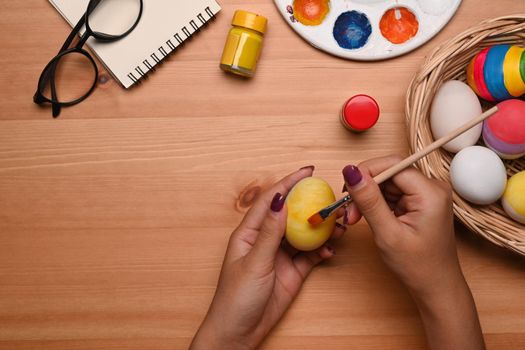Above view young woman holding paintbrush and coloring egg. Happy Easter concept.