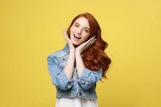 Lifestyle Concept: Smiling beautiful young woman in jean clothes posing with hands on chin. Isolated over yellow background