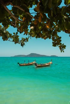 Fishing boats on the coast of the sea in Thailand on the island of Phuket. Andaman sea calm azure clean transparent magical white sand. On the shore are huge white yellow rock stones.green palm trees