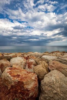 Colorful stones on a shore with stormy clouds at the horizon. Vertical view