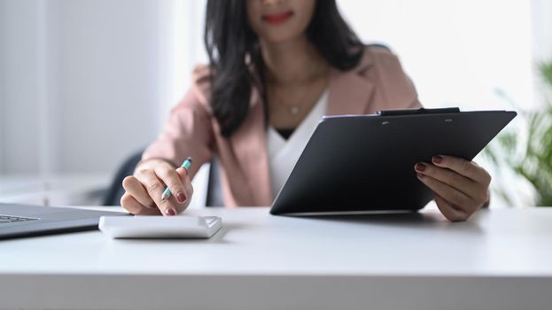 Focused professional female accountant is using calculator at office desk.
