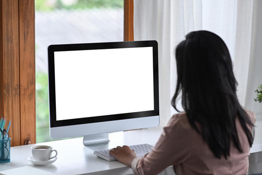 Rear view of businesswoman using computer at bright modern workplace.