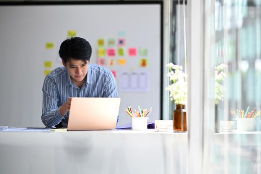 Young asian male web developer working on mobile application software design project at modern workplace.