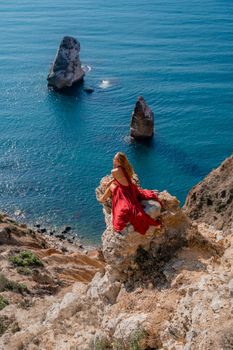 A girl with flowing hair in a long red dress sits on a rock above the sea. The stone can be seen in the sea