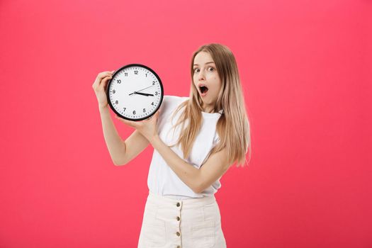 Amazed woman holding clock. Surprised woman in white t-shirt holds black clock. Retro style. Saving time concept. Summer sale. Discount. Isolated on pink background