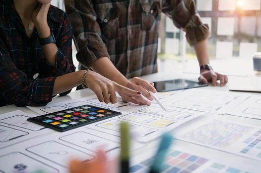 Web developers discussing and planning interface of mobile website with layouts on table.