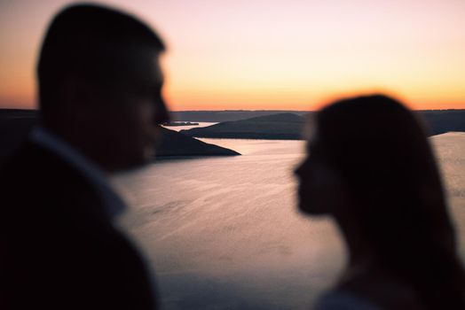 Silhouettes of bride and groom in wedding dress at night against backdrop of large lake and islands. Bakota, Ukraine