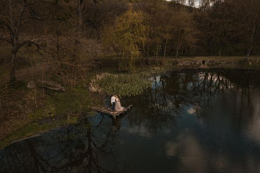 married couple a man with a pregnant woman with a big belly stand on a wooden bridge on coast lake river in nature. Aerial drone top view