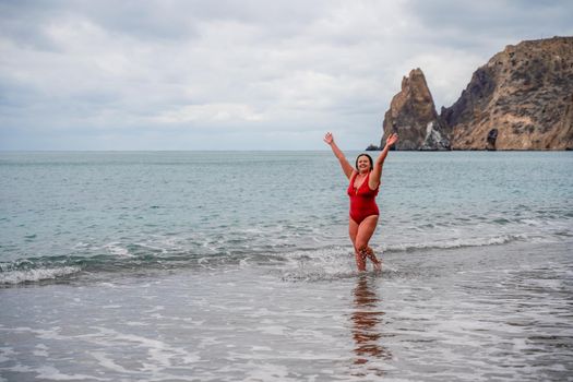 Woman in a bathing suit at the sea. A fat young woman in a red swimsuit enters the water during the surf.