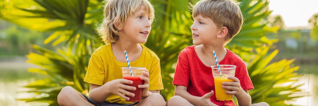 BANNER, LONG FORMAT Two boys drink healthy smoothies against the backdrop of palm trees. Mango and watermelon smoothies. Healthy nutrition and vitamins for children.