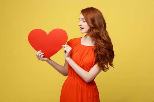Lifestyle and Holiday Concept - Portrait Young happy red hair woman in orange beautiful dress holding big red heart paper