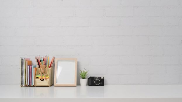 Creative workplace with empty frame, camera and stationery on white table with copy space.