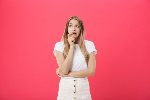 Close-up portrait of a young woman scared ,afraid and anxious biting her finger nails, looking to the camera, with wide opened eyes isolated on a pink background. Human emotions.