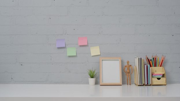 Home office desk with picture frame, potted plant, stationery and colorful sticky notes on brick wall background.
