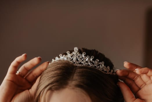 the girl holds on her head a tiara crown decorated with precious stones, young woman bride straightens accessories on her head and ears