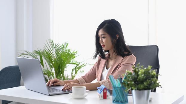 Concentrated young female entrepreneur checking email on her laptop computer.