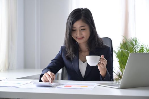 Professional financial advisor drinking coffee and checking reports at office desk.