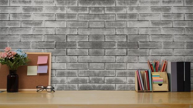 Stylish workplace with books, pencil holder and flower pot on wooden table against brick wall. Copy space for your advertise text.