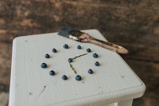 Fresh blue matte round blueberries. on wooden white chairs lie berries folded in a circle in the shape of a clock. blue paint brush