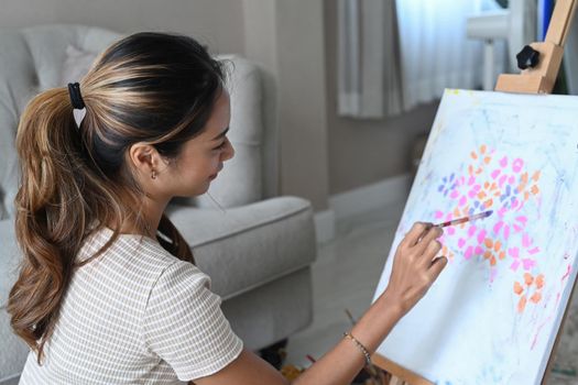 Beautiful woman sitting in front of easel and painting picture with watercolor.