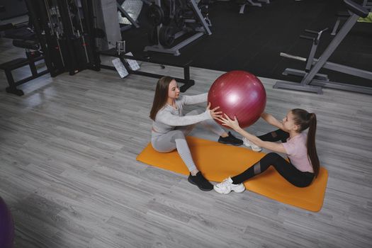 Top view shot of a teen girl working out with fitness trainer at the gym, doing situps with fit ball