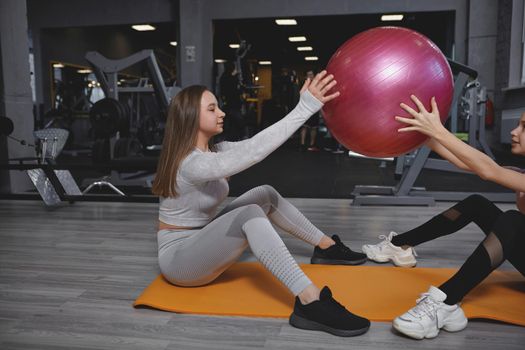 Fitness trainer exercising with her teen client, doing fit ball sit ups