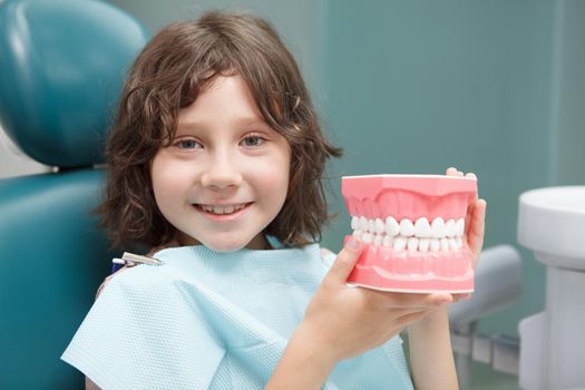 Close up of adorable little boy smiling, holding dental model, sitting at dentists office