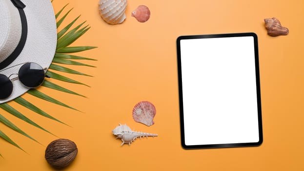 Above view digital tablet, traveler accessories and seashells on yellow background. Travel, summer and holiday concept.