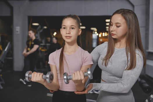 Personal trainer helping her teenage client lifting weights at the gym