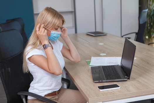 Woman putting on her protective face mask, working at the office during coronavirus pandemic