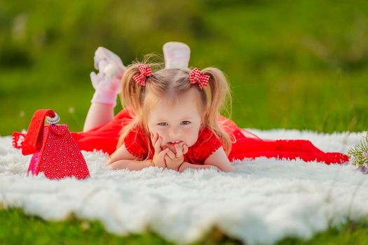 a girl in a red dress lies on a white blanket that is laid on the lawn