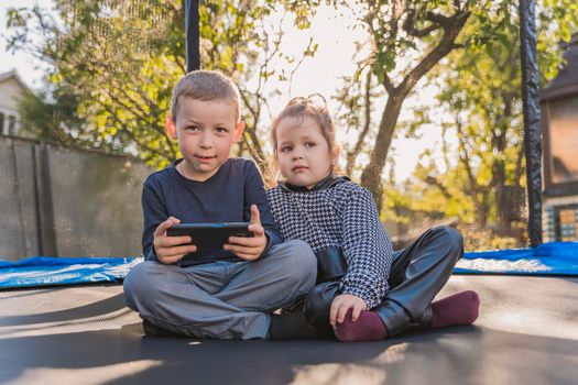 children look at the phone while sitting on a trampoline