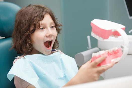 Close up of a happy young boy playing with big jaw model at dental clinic