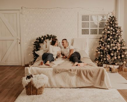 couple man and woman lie on bed bedroom near christmas tree.decorated house for New Year.Christmas morning. apartment interior. Valentine's Day celebration