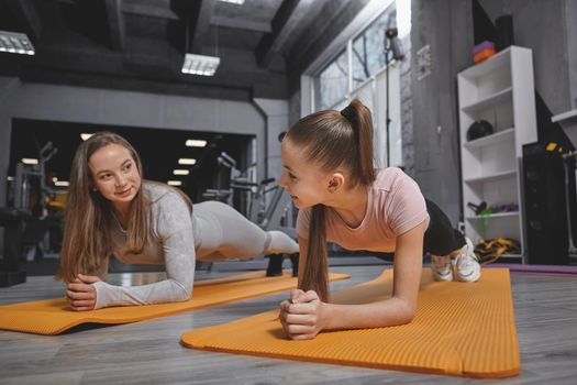 Teen girl enjoying working out at the gym with personal trainer, doing plank exercise