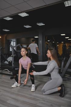 Vertical full length shot of a teenage girl doing squats with weights, her personal trainer supervising