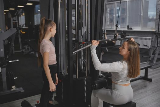 Personal trainer teaching teen girl working out on lat pull down gym machine