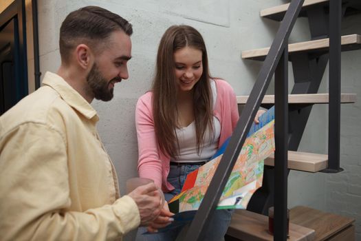 Young beautiful woman sitting on staircase at the hotel room, showing her boyfriend city map