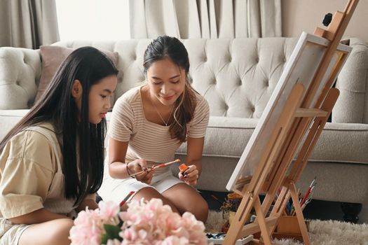 Happy young woman enjoy painting picture with her young sister at home.