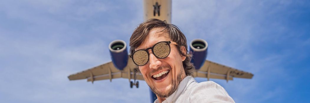 A man takes a selfie against the sky and a flying plane. BANNER, LONG FORMAT